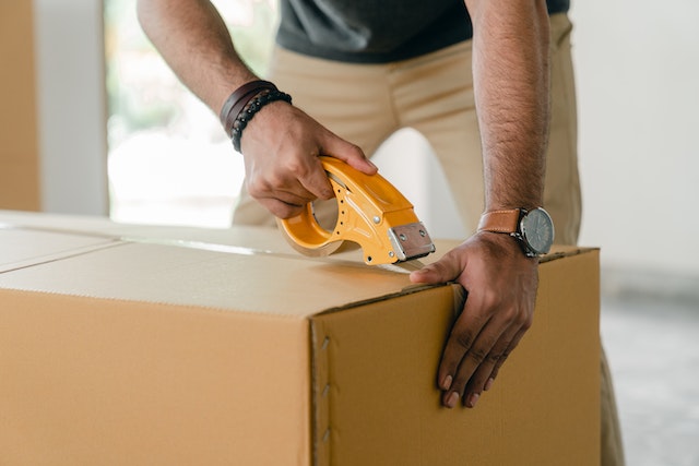Cropped image of a person taping a cardboard moving box closed